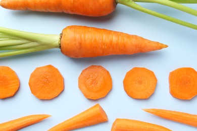 Whole and cut fresh carrots on light background, flat lay