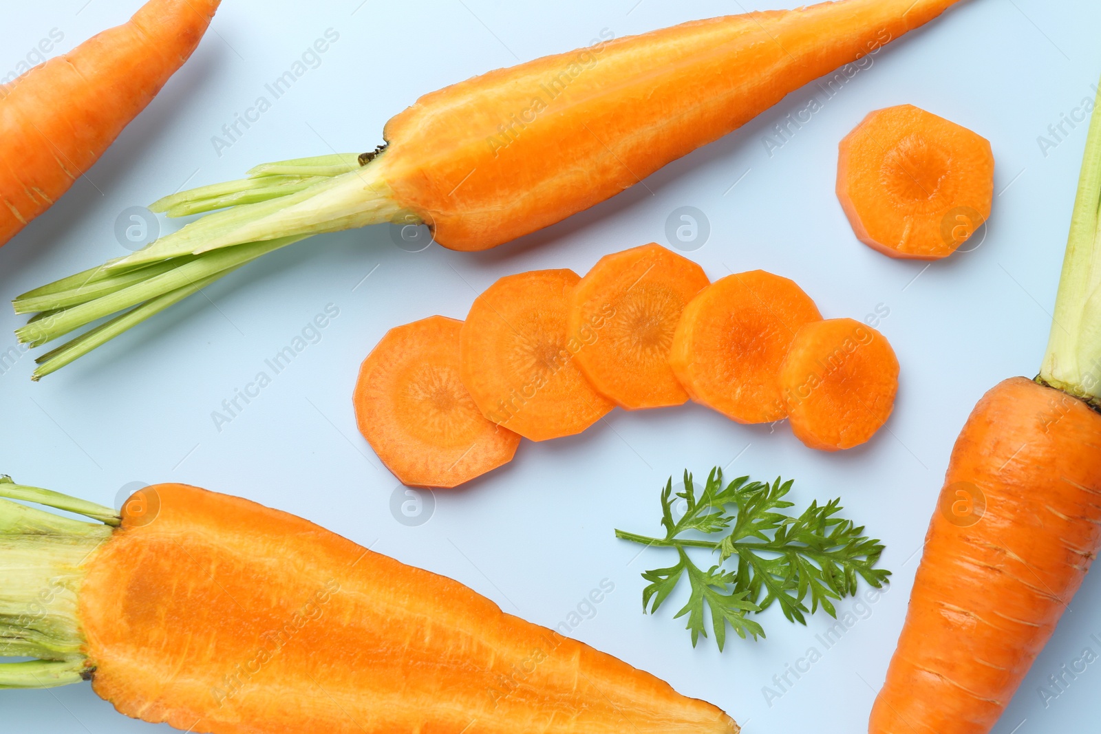 Photo of Whole and cut fresh carrots with green leaf on light background, flat lay