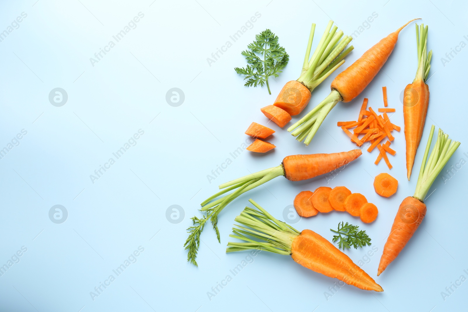 Photo of Whole and cut fresh carrots with green leaves on light background, flat lay. Space for text