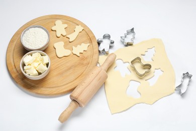 Photo of Raw dough, cookie cutters, board, ingredients and rolling pin on white background, above view