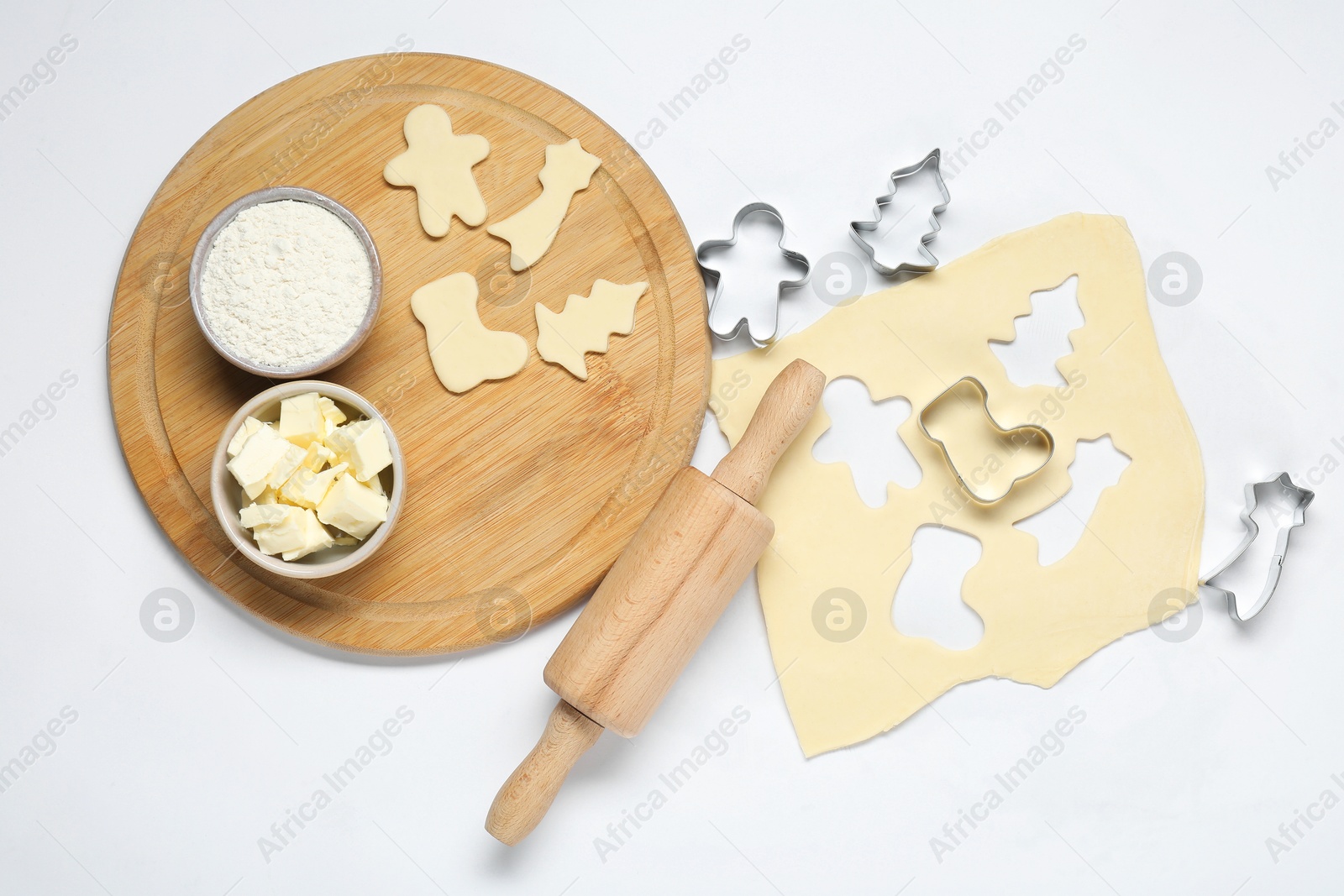 Photo of Raw dough, cookie cutters, board, ingredients and rolling pin on white background, flat lay