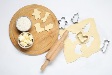 Photo of Raw dough, cookie cutters, board, ingredients and rolling pin on white background, flat lay