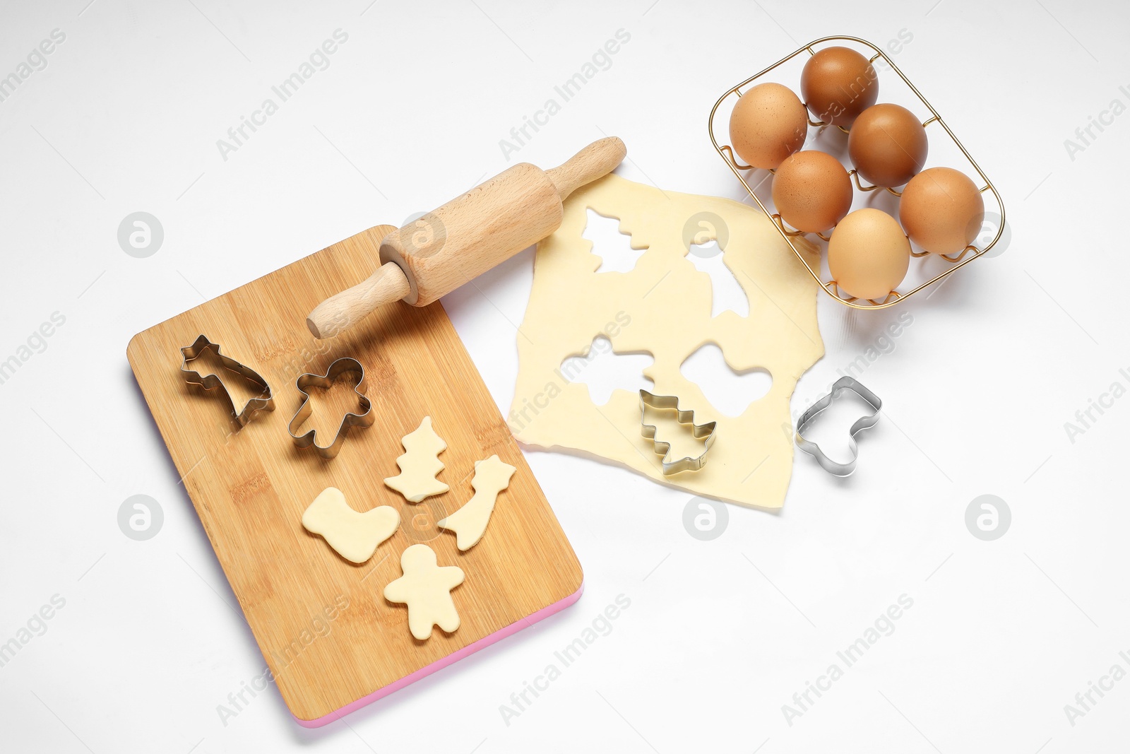 Photo of Raw dough, cookie cutters, board, eggs and rolling pin on white background, flat lay