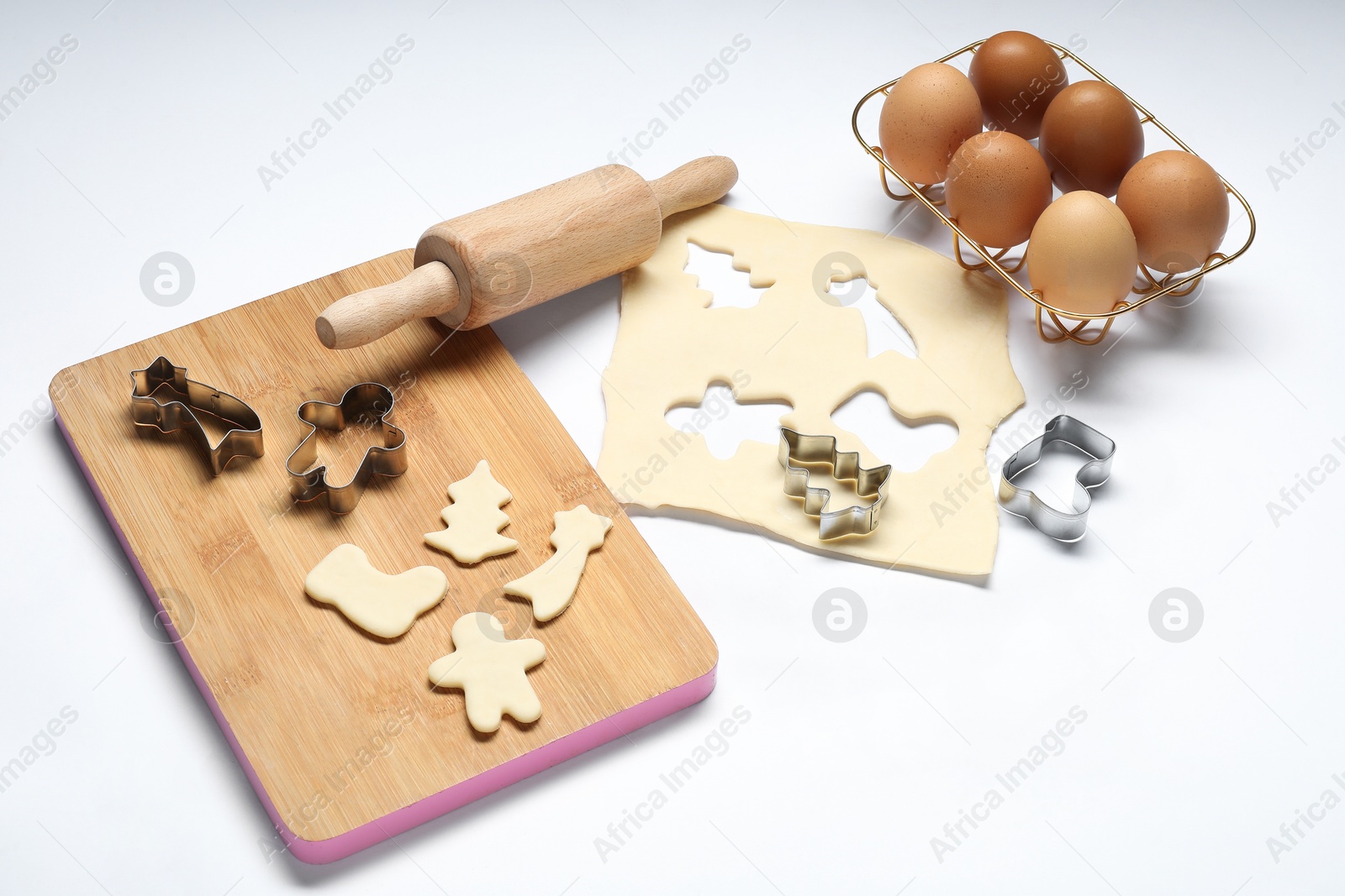 Photo of Raw dough, cookie cutters, board, eggs and rolling pin on white background