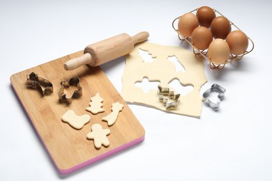 Raw dough, cookie cutters, board, eggs and rolling pin on white background