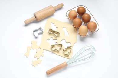 Raw dough, cookie cutters, whisk, eggs and rolling pin on white background, flat lay