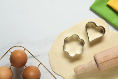 Photo of Raw dough, cookie cutters, eggs and rolling pin on white marble table, flat lay