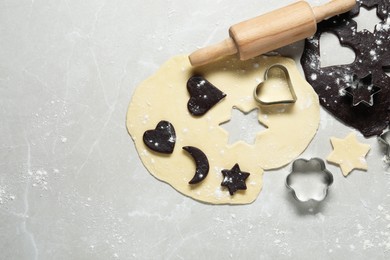 Raw doughs, rolling pin and cookie cutters on light marble table, flat lay. Space for text