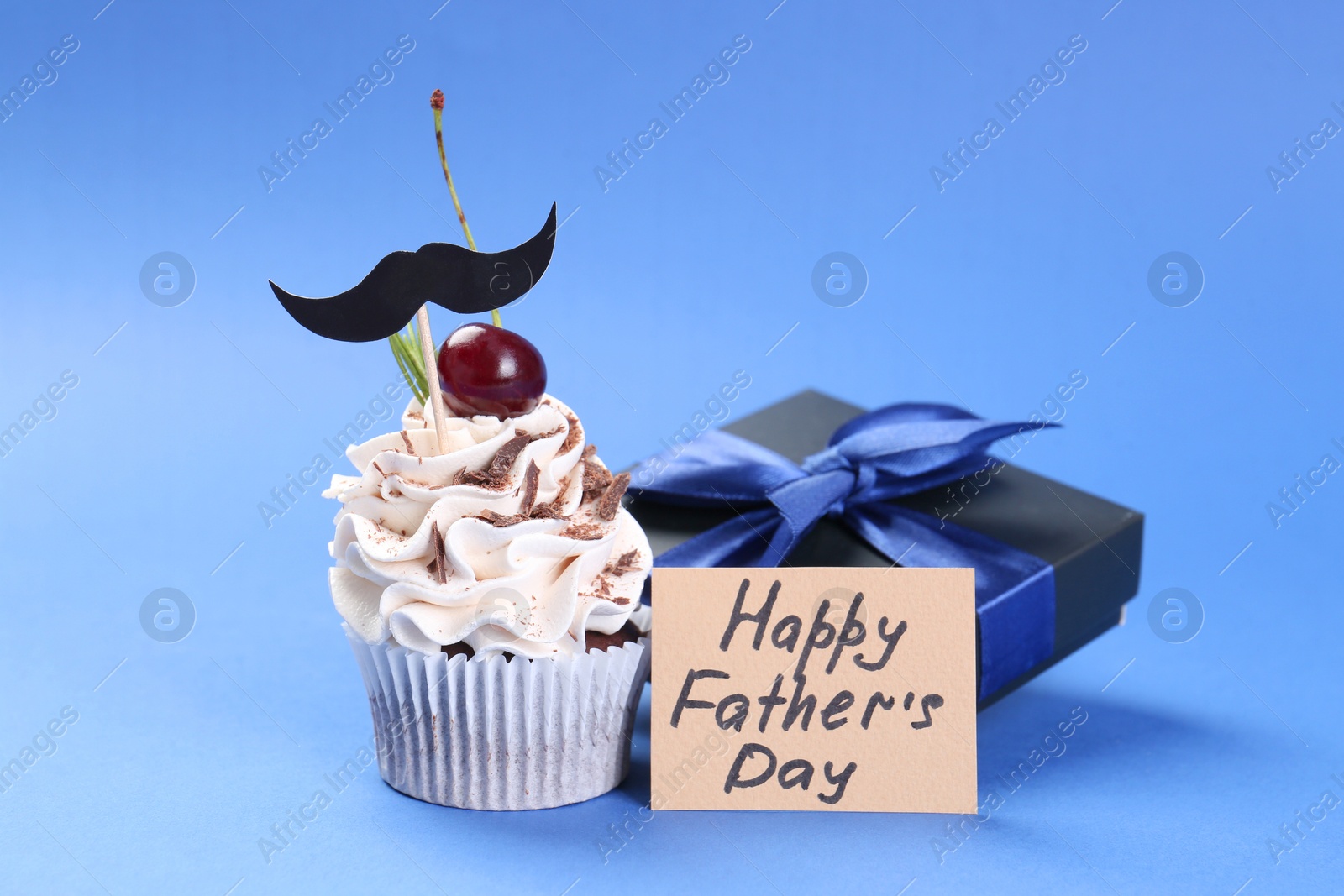 Photo of Gift box, card with phrase Happy Father's Day and cupcake with mustache topper on blue background, closeup