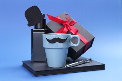 Photo of Happy Father's Day. Cup with paper mustache, notebook, pen, perfume and gift box on blue background, closeup