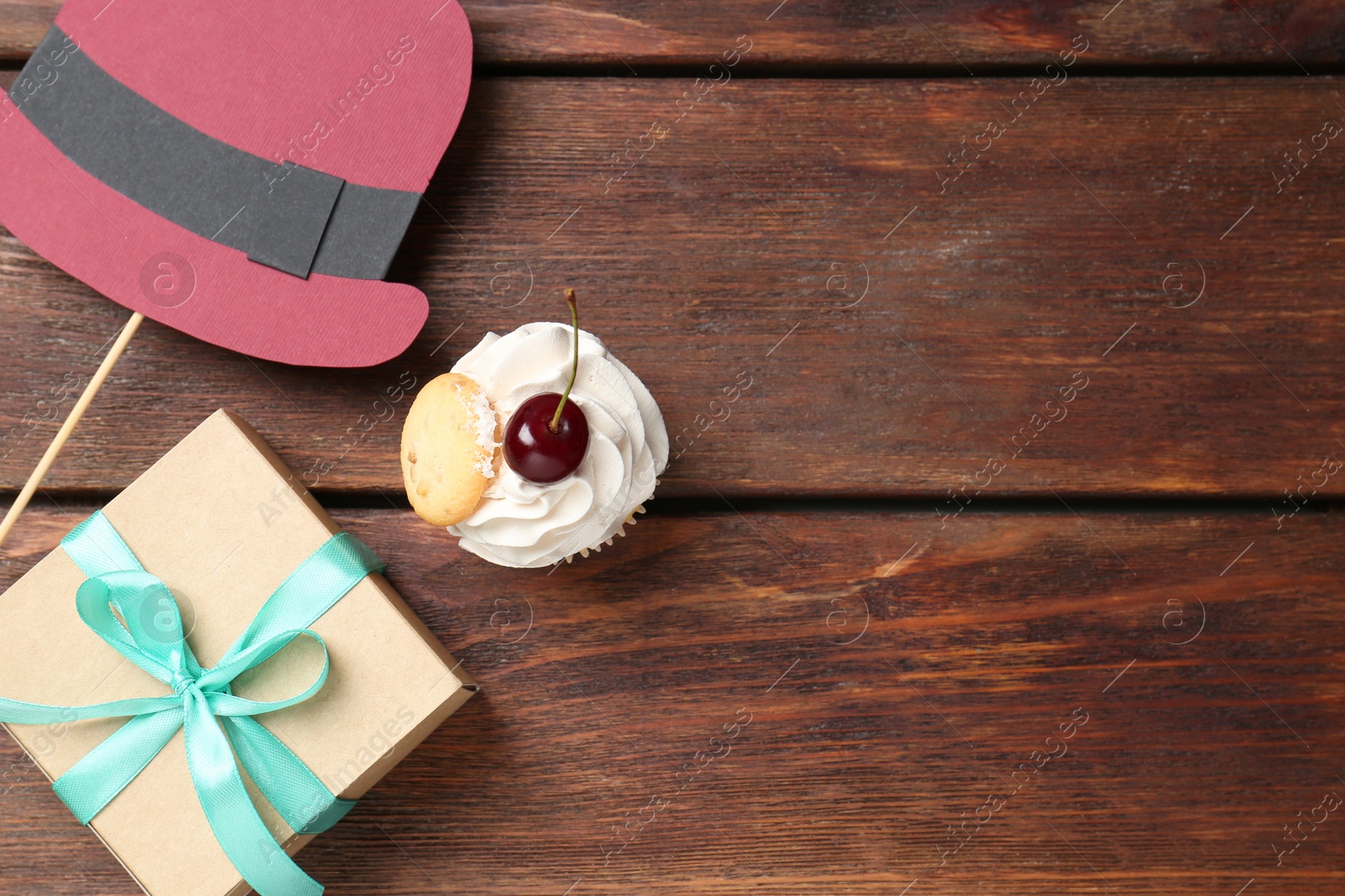 Photo of Happy Father's Day. Cupcake, paper hat and gift box on wooden table, flat lay. Space for text