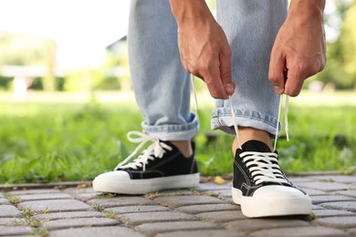 Photo of Man tying shoelace of black sneaker outdoors, closeup. Space for text