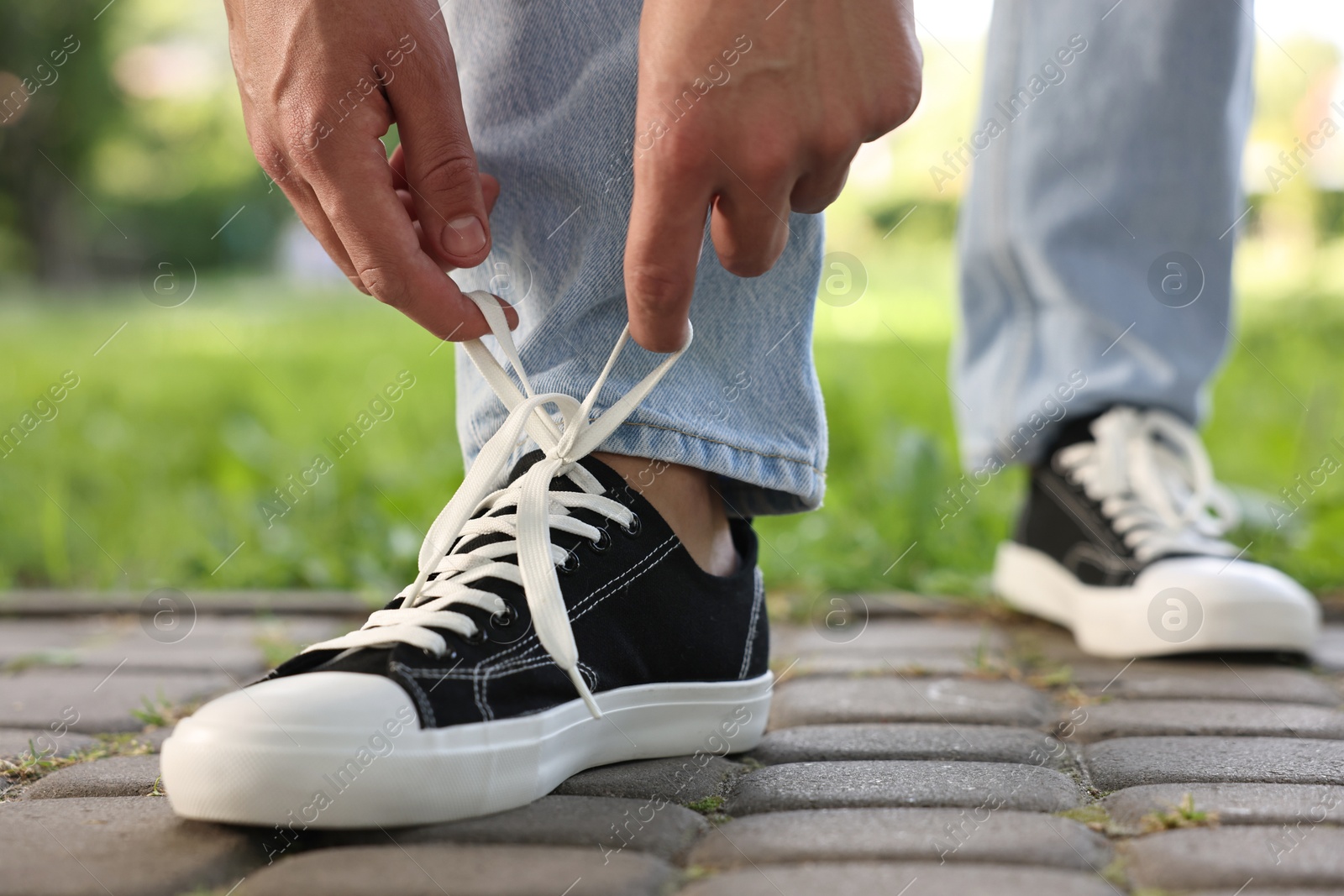 Photo of Man tying shoelace of black sneaker outdoors, closeup