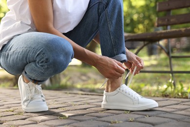 Woman tying shoelace of white sneaker outdoors, closeup