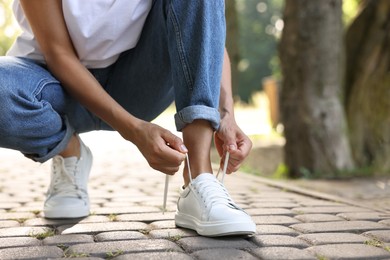 Photo of Woman tying shoelace of white sneaker outdoors, closeup. Space for text