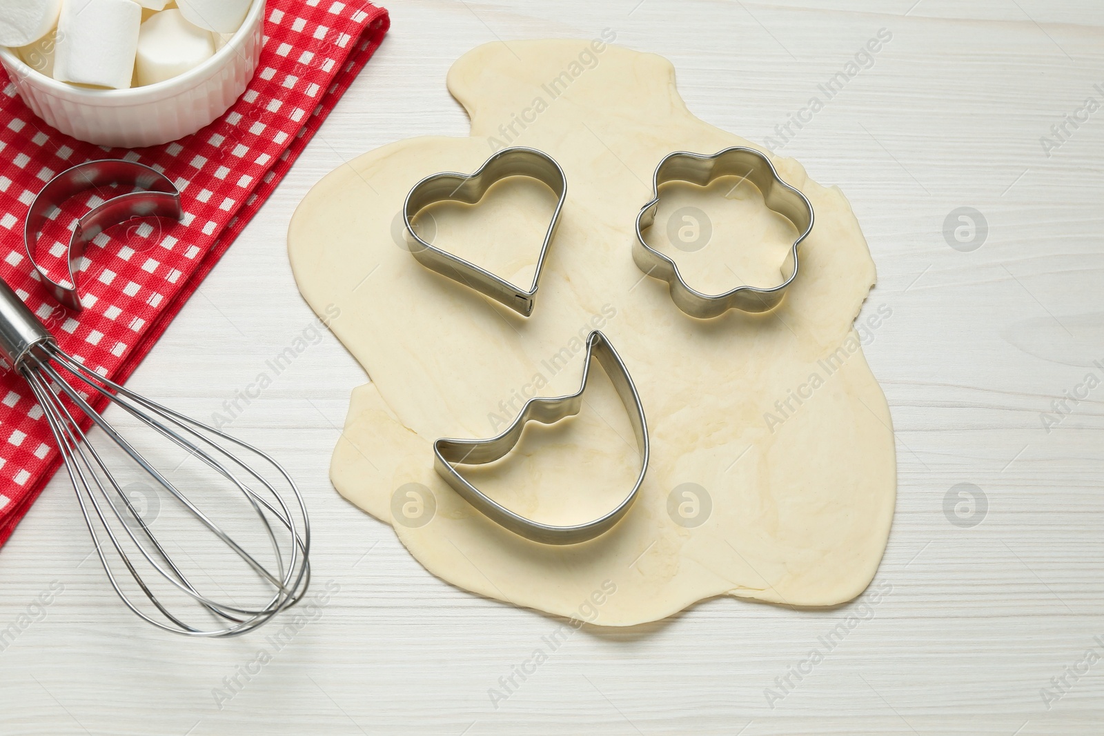 Photo of Raw dough, cookie cutters and whisk on white wooden table, above view