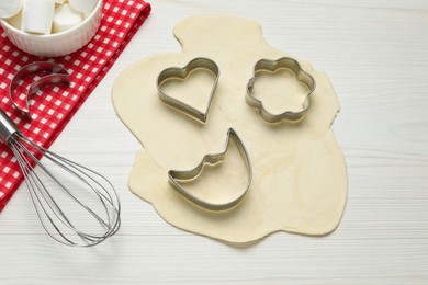 Photo of Raw dough, cookie cutters and whisk on white wooden table, above view