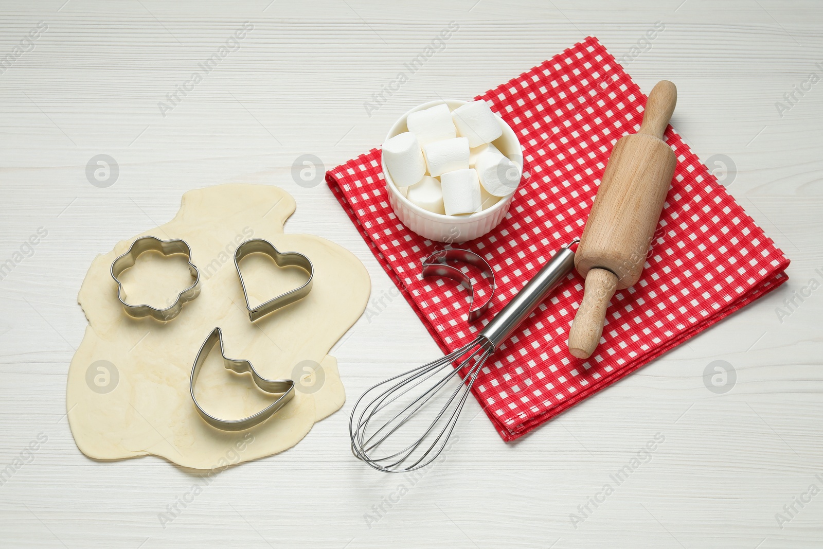 Photo of Raw dough, cookie cutters, whisk and rolling pin on white wooden table, above view