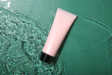 Cosmetic product. Tube with cream in water on green background, top view