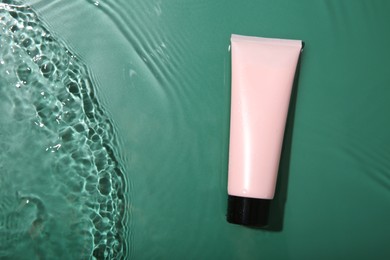 Photo of Cosmetic product. Tube with cream in water on green background, top view. Space for text