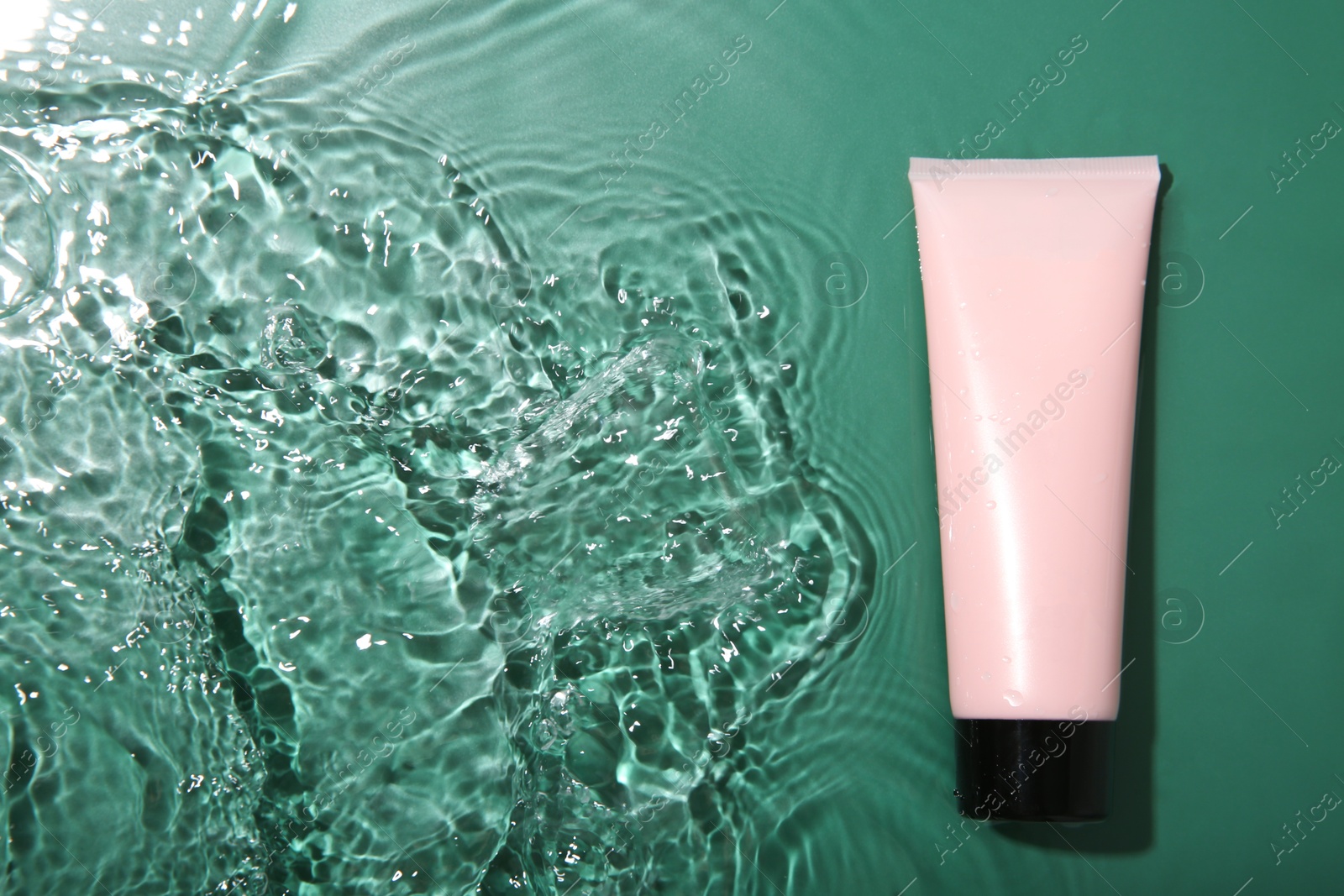 Photo of Cosmetic product. Tube with cream in water on green background, top view. Space for text