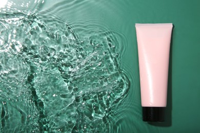 Cosmetic product. Tube with cream in water on green background, top view. Space for text