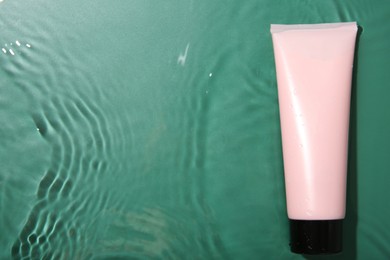 Cosmetic product. Tube with cream in water on green background, top view. Space for text