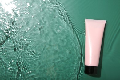 Cosmetic product. Tube with cream in water on green background, top view. Space for text