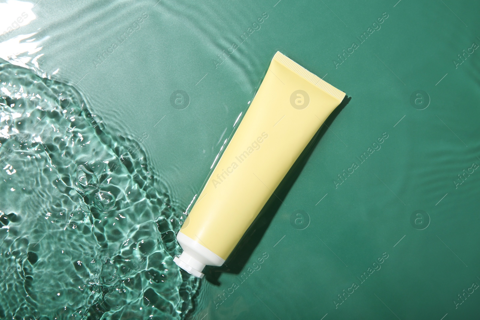 Photo of Cosmetic product. Tube with cream in water on green background, top view