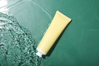 Cosmetic product. Tube with cream in water on green background, top view