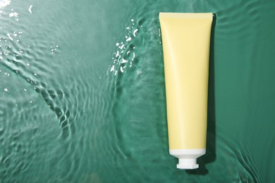 Cosmetic product. Tube with cream in water on green background, top view. Space for text