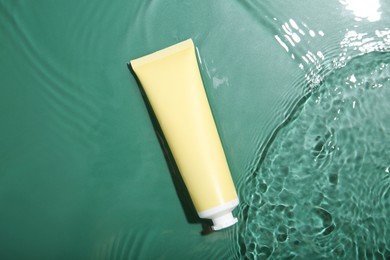 Cosmetic product. Tube with cream in water on green background, top view