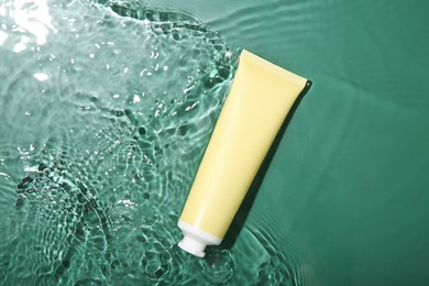 Photo of Cosmetic product. Tube with cream in water on green background, top view