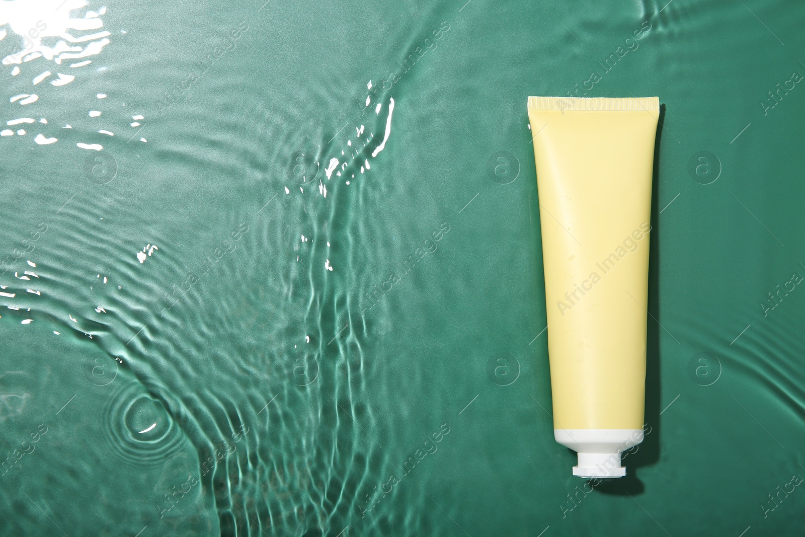 Photo of Cosmetic product. Tube with cream in water on green background, top view. Space for text