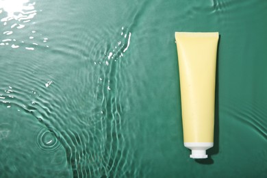 Photo of Cosmetic product. Tube with cream in water on green background, top view. Space for text