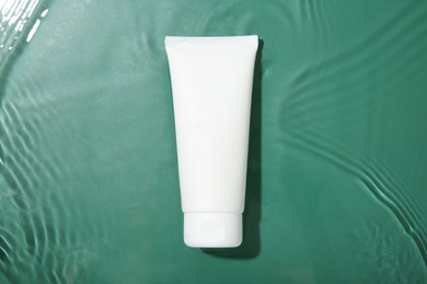 Photo of Cosmetic product. Tube with cream in water on green background, top view