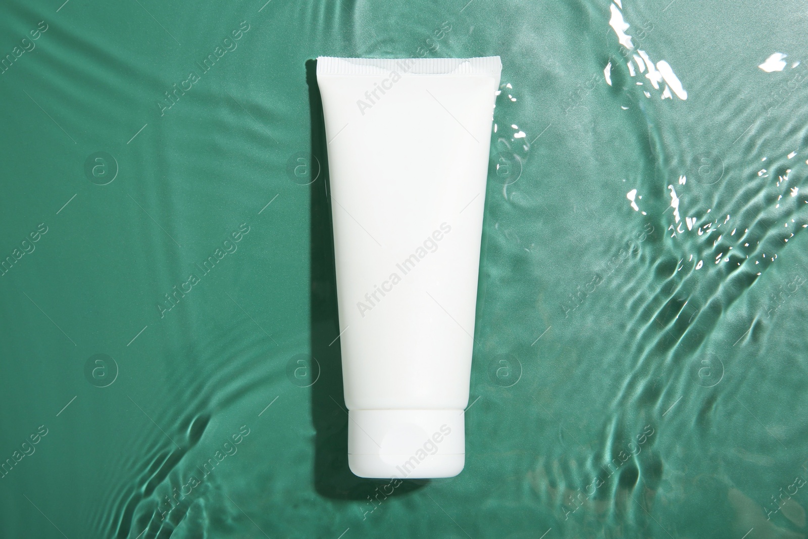 Photo of Cosmetic product. Tube with cream in water on green background, top view