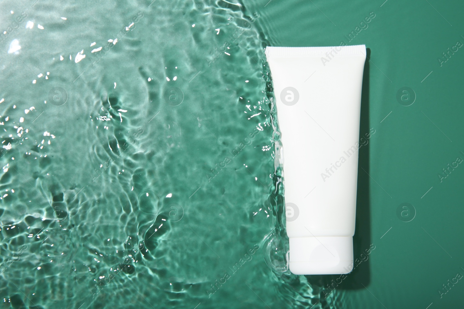 Photo of Cosmetic product. Tube with cream in water on green background, top view. Space for text