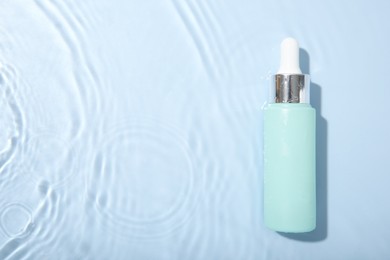 Photo of Bottle of cosmetic product in water on light blue background, top view. Space for text