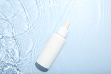 Bottle of cosmetic product in water on light blue background, top view