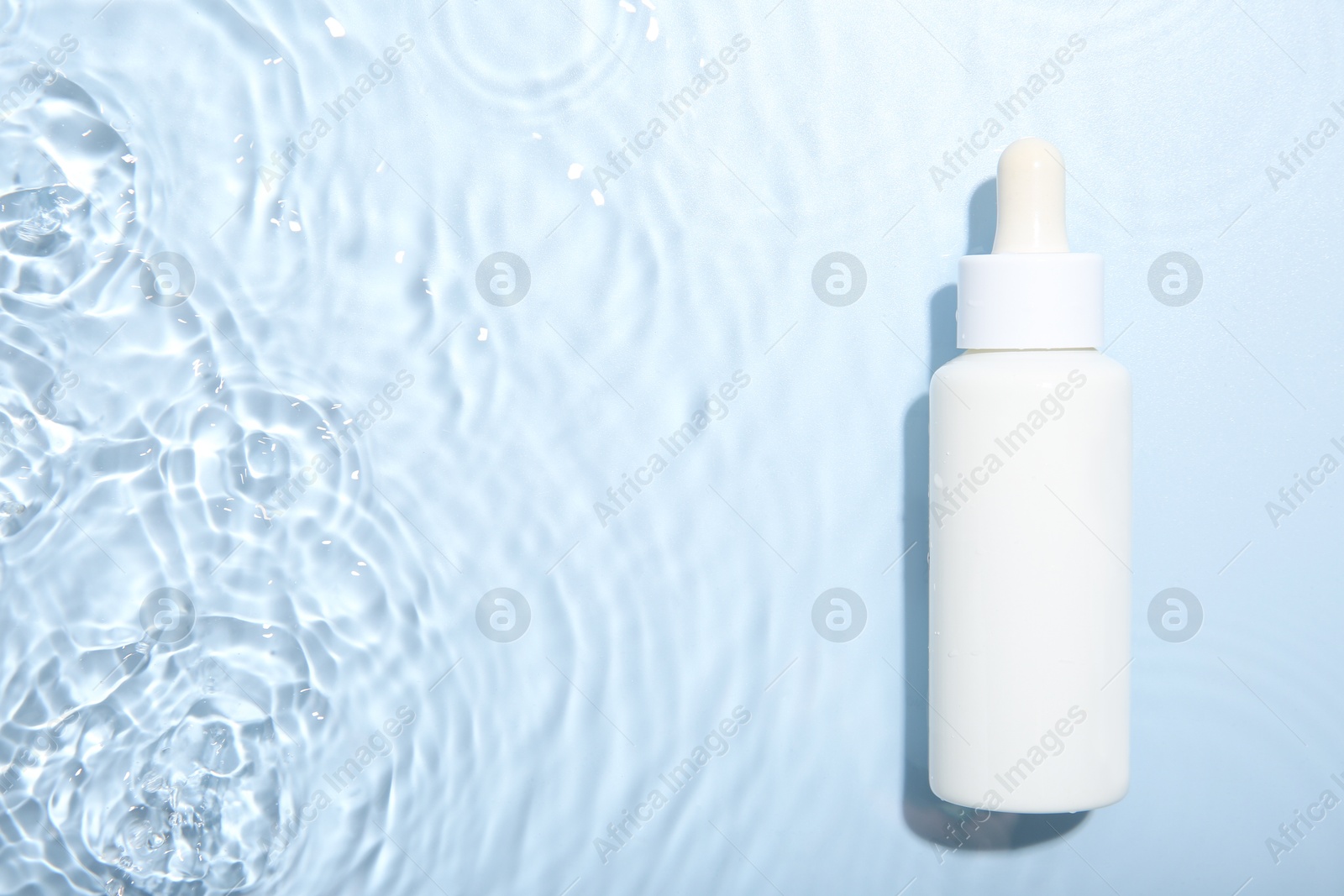 Photo of Bottle of cosmetic product in water on light blue background, top view. Space for text