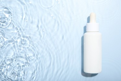 Bottle of cosmetic product in water on light blue background, top view. Space for text