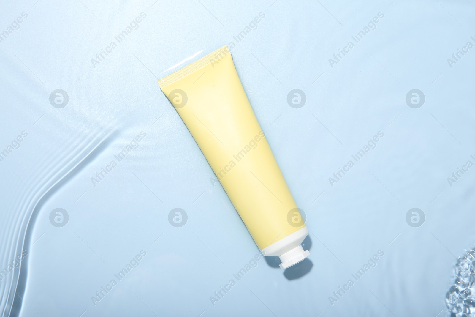 Photo of Cosmetic product. Tube with cream in water on light blue background, top view