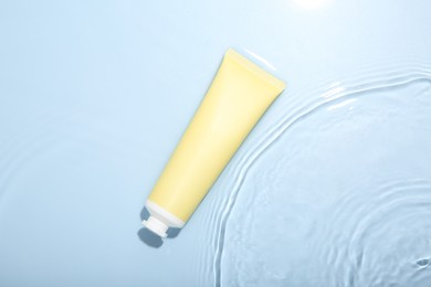 Photo of Cosmetic product. Tube with cream in water on light blue background, top view