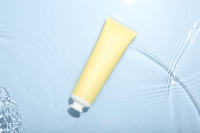 Photo of Cosmetic product. Tube with cream in water on light blue background, top view