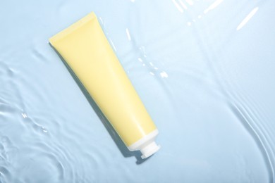 Cosmetic product. Tube with cream in water on light blue background, top view