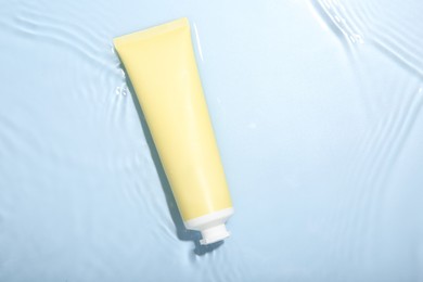 Photo of Cosmetic product. Tube with cream in water on light blue background, top view