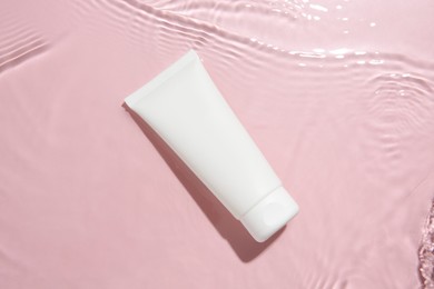 Photo of Cosmetic product. Tube with cream in water on pink background, top view