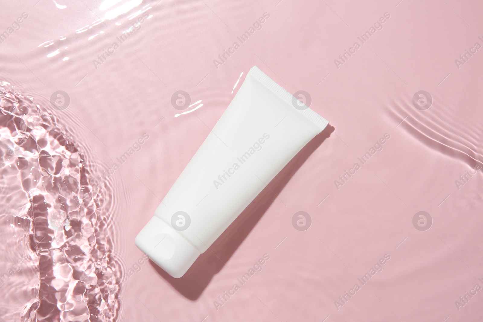 Photo of Cosmetic product. Tube with cream in water on pink background, top view