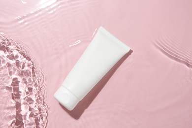 Photo of Cosmetic product. Tube with cream in water on pink background, top view